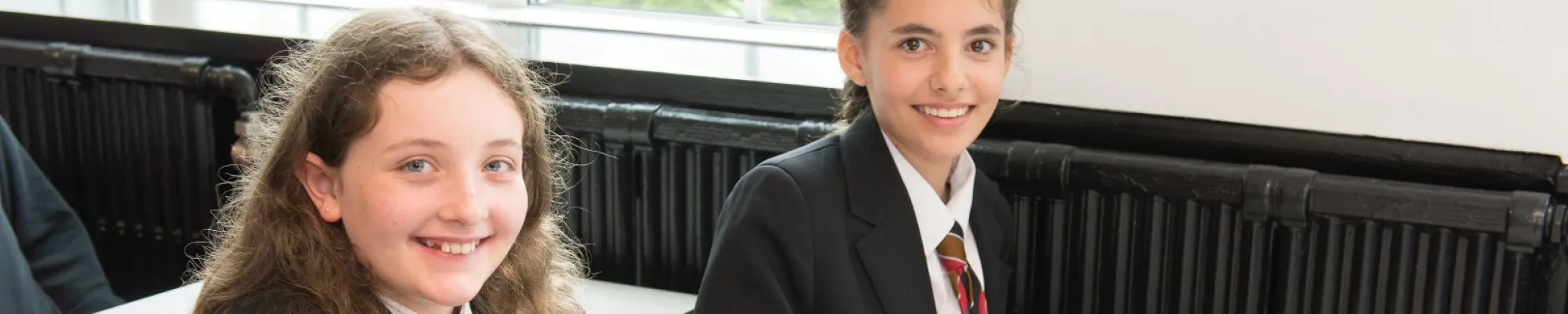 Two pupils smiling sitting at a desk